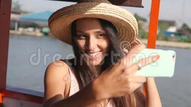 年轻快乐混血旅游妇女漂浮在木制泰国船和自拍照片使用手机。 泰国